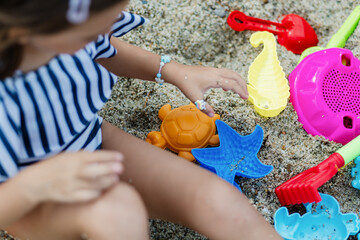 Child enjoys playing with colorful sand toys while sitting on the beach in a sunny summer afternoon