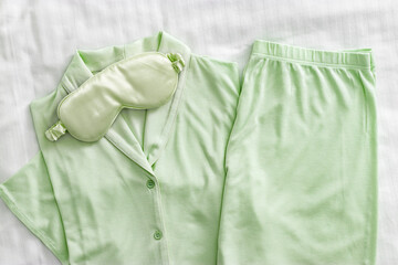 Pajama Set with silk sleep mask pastel green colored on white sheet. Top view fashion woman home sleepwear from natural cotton on bedclothes. Cozy pyjamas of shirt and shorts for comfort dream