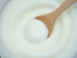 Wooden Spoon Scooping Thick White Yogurt in Swirling Pattern Smooth Texture Background