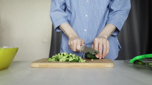 Close up of a person chopping fresh cucumber on a wooden cutting board in the kitchen, concept of healthy eating, vegetarian meal preparation, and home cooking routine