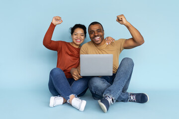 Excited African American couple sitting with laptop, cheering with joy. Portrait representing digital success, teamwork, love, and happiness in modern lifestyle