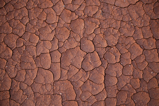 Dry, red-brown, cracked and dusty ground surface. Soil erosion. Cracked red clay top view