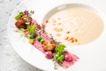 Gourmet soup with artistic plating, featuring colorful garnishes, microgreens, and vibrant sauces on a white dish. Fine dining presentation in modern culinary style.