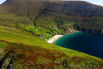 Aerial view of Keem Beach with calm blue Atlantic waters, cars parked along the road, and a winding mountain road in County Mayo	