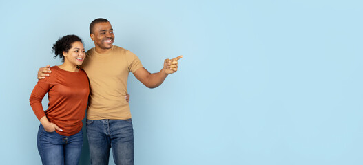 Happy African American couple standing close together in studio, smiling and pointing at copy space. Casual portrait of love, partnership, and joyful lifestyle expression