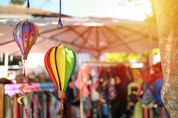 Colorful hot air balloons are suspended among market stalls, creating a festive atmosphere during a sunny day at a local craft fair