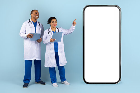 African American doctors in studio with large smartphone mockup. Smiling medical team presenting healthcare mobile app solution, innovation and technology in medicine - Powered by Adobe