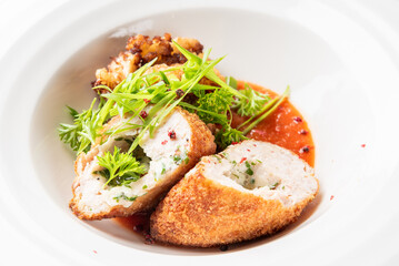 Stuffed breaded chicken breast sliced open, served over tomato sauce, garnished with herbs, green onions, and red peppercorns. Gourmet plated dish, top view.
