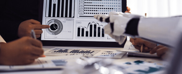 A dynamic business meeting showcasing data visualization with a human and robot collaboration, emphasizing technology and innovation in a modern office environment.Noogenesis