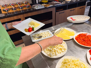 Person selecting cheese and vegetables at buffet with plate in hand. Lifestyle, hospitality, and nutrition in hotel breakfast environment.
