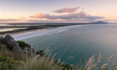 Fototapeta premium Coastal panorama at dawn, with a sandy beach stretching into a calm turquoise ocean, framed by rolling hills and a gentle sky