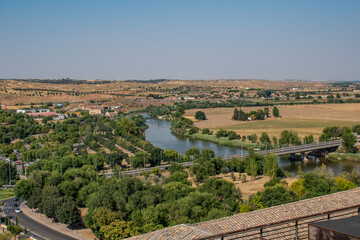 Landscape with fields, lush trees, and the Tagus River flowing through Toledo, Spain.