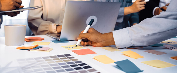 A dynamic office scene showcasing a diverse group of professionals engaged in a collaborative brainstorming session, utilizing laptops and colorful sticky notes for planning. SACTR