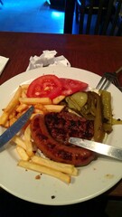 Plate of meal with fries, sausage, burger patty, tomatoes, pickles, and peppers