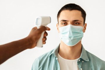 Health screening and protection against covid-19 epidemic in vaccination center. African american doctor or nurse taking body temperature with infrared thermometer at patient in clinic, free space