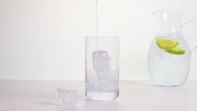 Trinkglas mit Mineralwasser und Limonenscheibe und Eisw&uuml;rfeln