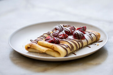 Crepes with chocolate drizzle and fresh strawberries on a plate. Delicious pancake with strawberry and chocolate cream on the plate. 