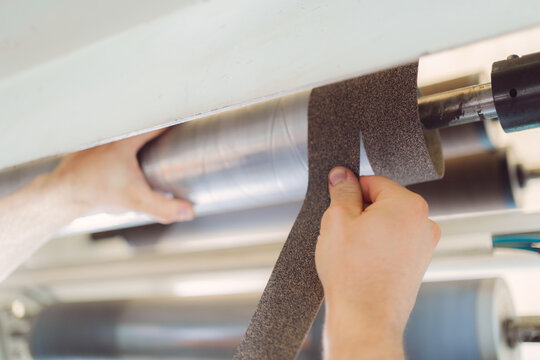 Close-up of worker hands adjusting sandpaper on a roller in an industrial sanding machine, precision work process.