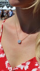 A woman wearing a necklace with a blue stone pendant. The necklace is gold and the woman is wearing a red floral dress