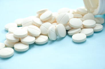 Close-up of round white tablets scattered on a blue background with an open container.