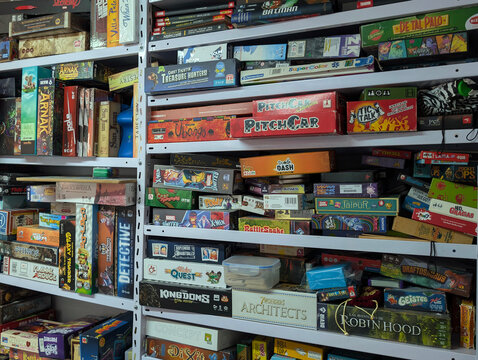 Large collection of board games of various genres in shelves. Tabletop, strategy, fantasy, cooperative, adventure, role-playing, card, family, war game genre variety. Hobby, gamer leisure. 