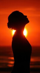 A woman is standing on the beach, looking up at the sun. The sun is setting, casting a warm glow over the scene. The woman is in a contemplative or meditative state