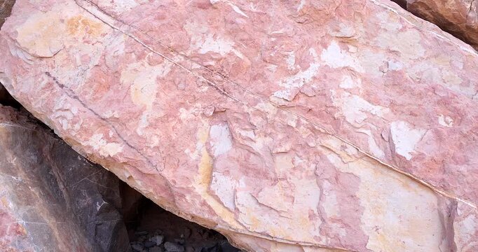 Closeup rough oval shaped pink rock with white mineral layers and blotches in dry stack wall 4k