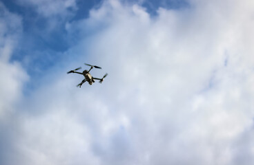 A drone takes pictures from the sky, drone reconnaissance, on a blue sky background. Flying drone on the sky with clouds. An unmanned aerial vehicle ( UAV ) or quadcopter drone fly with four rotors. 