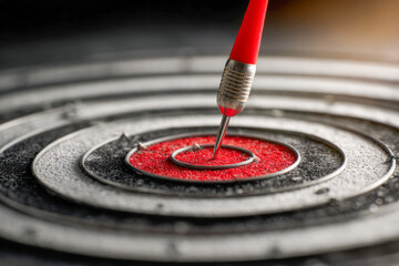Macro shot of a red dart perfectly hitting the bullseye on a textured black and red dartboard symbolizing precision and goal achievement in sports or business contexts