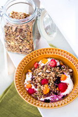 Homemade granola in a jar and on yogurt on an orange deep dish