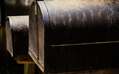 slightly angled view of several mailboxes supported on wooden posts. close up of weathered black letterboxes background with copy space