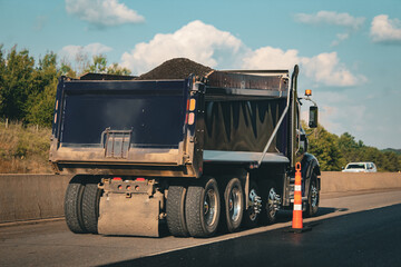 a multi-axle dump truck shown in a highway area with new asphalt. vehicles designed for transporting loose materials such as sand, gravel, dirt, and construction debris