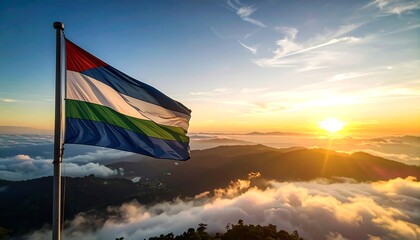 A national flag waves proudly in the sunlit sky over a mountainous, misty landscape, symbolizing freedom and sovereignty. Golden rays of light emanate from the rising sun