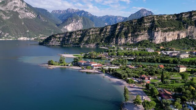 Stunning 4K aerial drone footage of Nago-Torbole and Torbole sul Garda on the northern shore of Lake Garda, Italy. Scenic view of the colorful town, mountains, beach, sailing boats