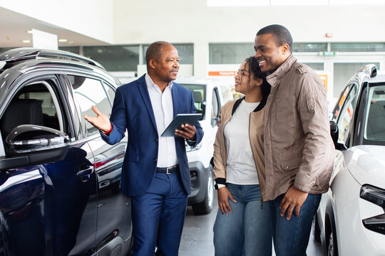 Happy black couple with dealer in showroom, cheerful discussion about SUV purchase, lifestyle concept of transport, modern business and finance auto shopping experience. - Powered by Adobe