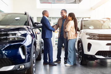 African American couple shaking hands with car dealer in showroom, celebrating successful agreement, lifestyle concept of vehicle purchase, trust, finance and ownership