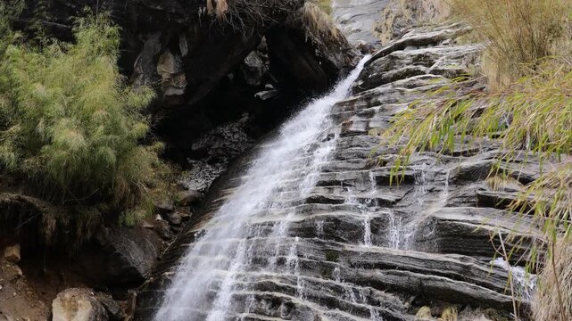 Real time video of waterfall stream falling from the cliff. Gray rocks in the river cascade of a high waterfall