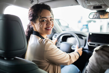 Smiling African American woman sitting in driver seat of new car, lifestyle concept of auto...