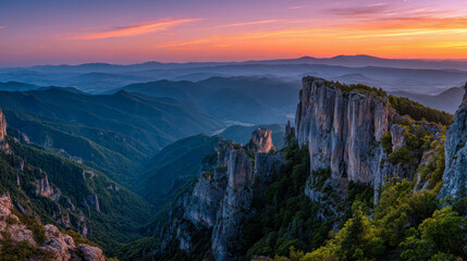 Fototapeta premium Stunning panoramic view of rugged mountain cliffs and dense forest valleys under a vibrant sunset sky with layered distant hills fading into the horizon