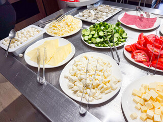 Plates with sliced cheese, vegetables, and cold cuts arranged on breakfast buffet table. Food, nutrition, and hospitality service in hotel dining area.