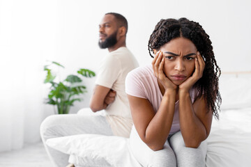 Upset millennial african american wife ignores offended husband on white bed in minimalist bedroom interior. Problems in bed, crisis in relationships, quarrel and scandal at home due COVID-19 pandemic