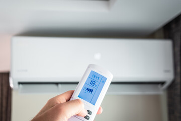 The man turns on the air conditioner with the remote control in his hand. The air conditioner is working in the cold.