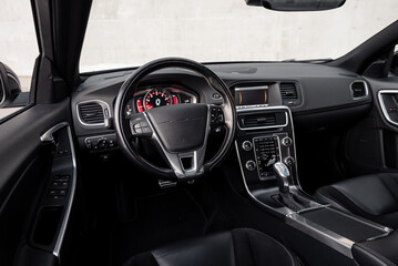 Interior of modern car. Car cockpit wide angle view: driver seat, steering wheel, center console and concrete wall in the background. 