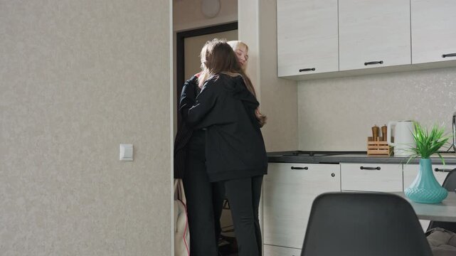 woman hugging sister upon return from trip as she drops handbag on chair and retrieves cheese snack placing it on table inside cozy kitchen with wooden cabinets and potted plant on table