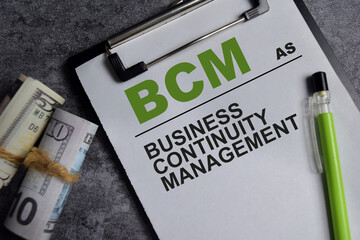 Concept of BCM - Business continuity management write on clipboard isolated on Wooden Table.