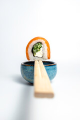 Elegant close-up shot of a salmon sushi roll balanced on chopsticks over a ceramic bowl, ideal for high-end restaurant websites or menu design.