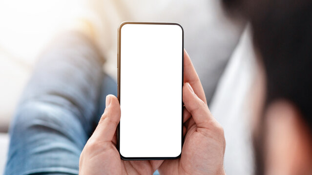 Reading books or blog and job search online. Unrecognizable man sitting on sofa and looking at smartphone with blank black screen, over the shoulder view, closeup