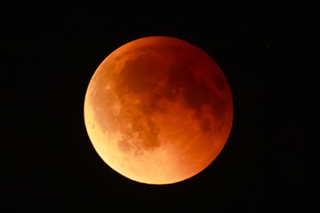 Close-up of a lunar eclipse, showing the Earths shadow covering the moon with a bright illuminated edge and reddish surface glow.