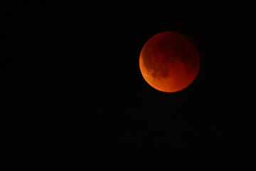 Close-up of a lunar eclipse, showing the Earths shadow covering the moon with a bright illuminated edge and reddish surface glow.