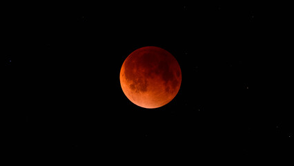 Blood moon during a lunar eclipse in the night sky. The moon appears red as it is shadowed by the Earth